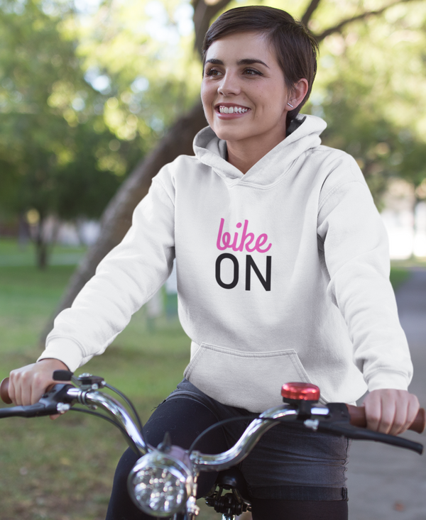 Frau mit weißem Bike ON Hoodie fährt Fahrrad durch einen Park – gemütlicher Kapuzenpullover für Radfahrer
